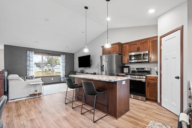 kitchen featuring light wood finished floors, a kitchen island, appliances with stainless steel finishes, a kitchen bar, and open floor plan