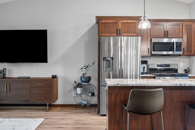 kitchen with pendant lighting, light stone counters, appliances with stainless steel finishes, light wood finished floors, and baseboards