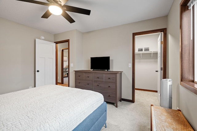 bedroom with a walk in closet, baseboards, light carpet, a closet, and a ceiling fan