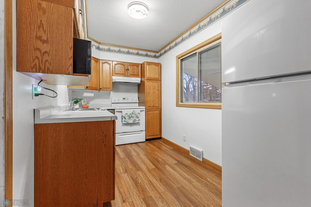 kitchen with a textured ceiling, white appliances, light hardwood / wood-style flooring, and sink