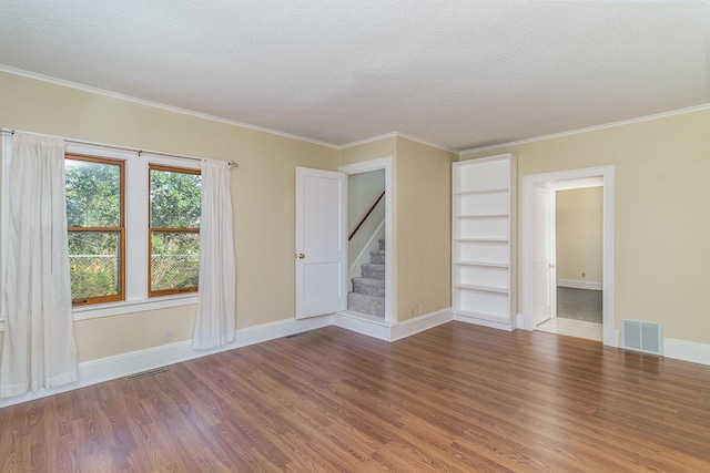 spare room featuring built in features, wood-type flooring, a textured ceiling, and ornamental molding