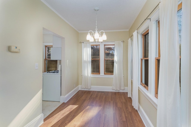 unfurnished dining area with a textured ceiling, hardwood / wood-style flooring, an inviting chandelier, and crown molding