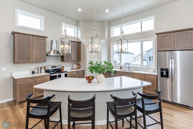 kitchen featuring stainless steel appliances, a kitchen island, light hardwood / wood-style floors, and wall chimney exhaust hood