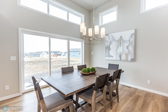 dining area featuring a towering ceiling, a chandelier, and light hardwood / wood-style floors