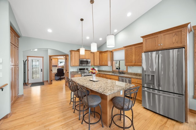 kitchen with appliances with stainless steel finishes, light wood-type flooring, sink, decorative light fixtures, and a kitchen island