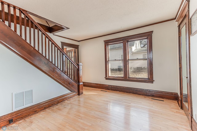 entryway featuring light wood-type flooring, a textured ceiling, and ornamental molding