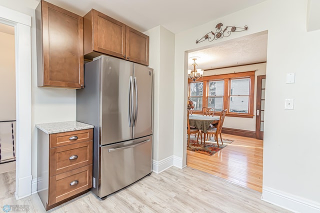 kitchen featuring light stone countertops, stainless steel fridge, light wood-type flooring, a textured ceiling, and a notable chandelier