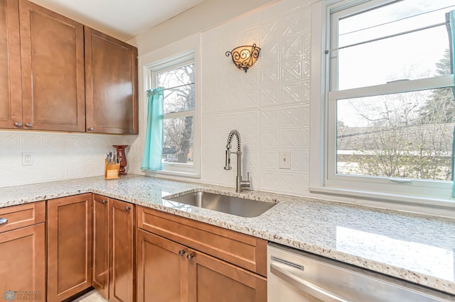 kitchen with stainless steel dishwasher, light stone counters, sink, and tasteful backsplash