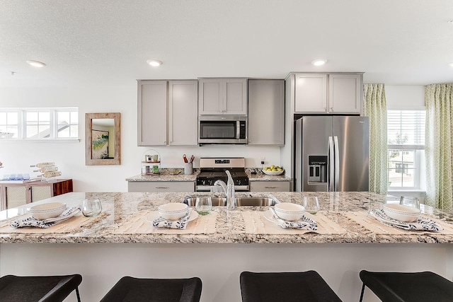 kitchen with stainless steel appliances, sink, a breakfast bar, and gray cabinetry