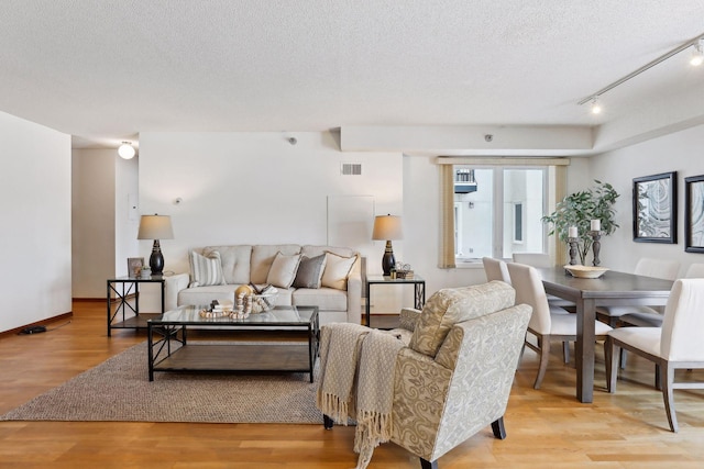 living room with a textured ceiling, light hardwood / wood-style floors, and track lighting