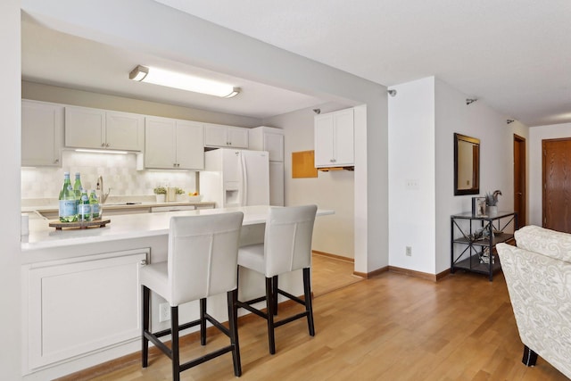 kitchen with backsplash, white cabinets, a kitchen breakfast bar, white fridge with ice dispenser, and kitchen peninsula