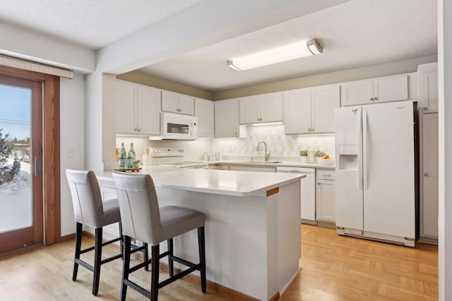 kitchen with white appliances, a kitchen breakfast bar, kitchen peninsula, a textured ceiling, and white cabinetry