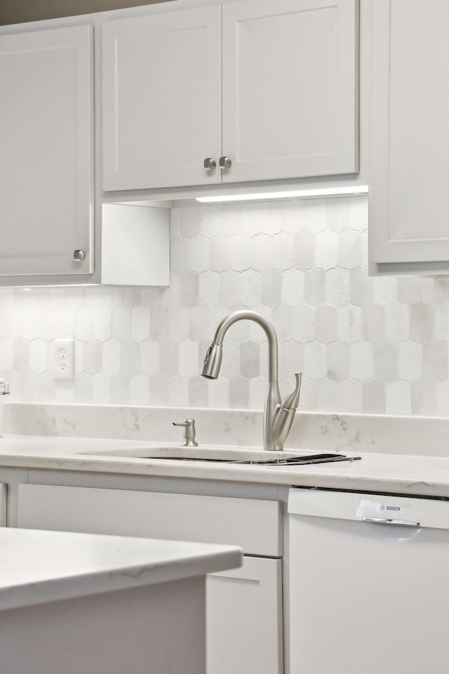 kitchen featuring white dishwasher, sink, white cabinets, and backsplash