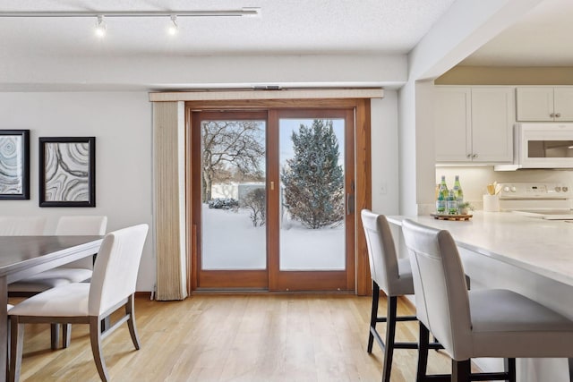 dining room with a textured ceiling, track lighting, and light hardwood / wood-style flooring