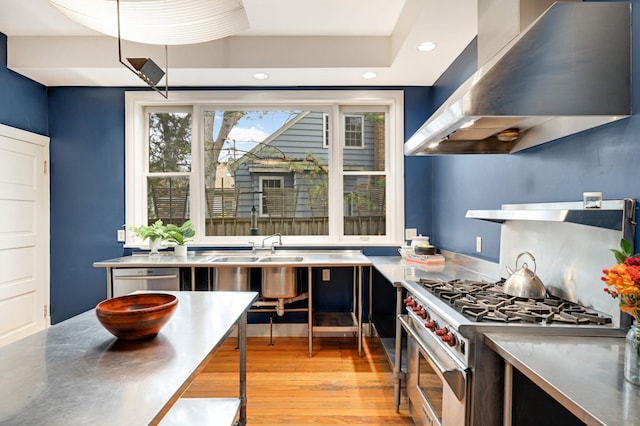 kitchen featuring appliances with stainless steel finishes, wall chimney range hood, light hardwood / wood-style flooring, and stainless steel counters