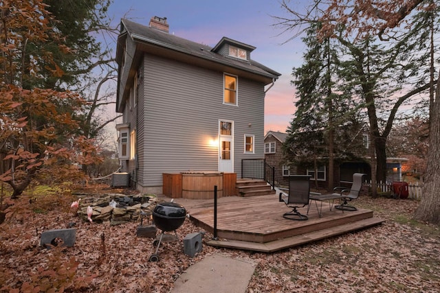 back house at dusk with an outdoor fire pit, a deck, and central AC