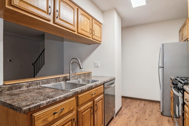 kitchen featuring light wood-type flooring, sink, appliances with stainless steel finishes, and dark stone counters