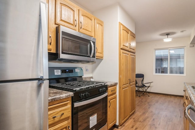 kitchen with light wood-type flooring, stainless steel appliances, and dark stone counters