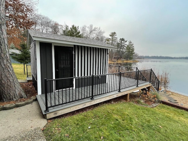 wooden terrace featuring an outbuilding, a water view, and a lawn