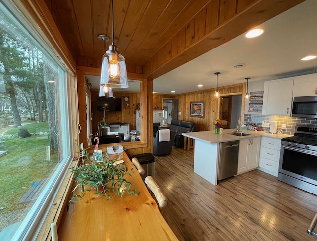 kitchen with decorative light fixtures, kitchen peninsula, a wealth of natural light, white cabinetry, and appliances with stainless steel finishes