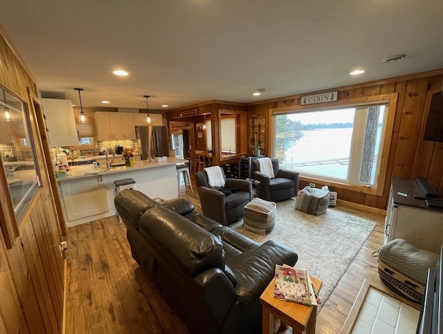 living room with sink, wood walls, and light wood-type flooring