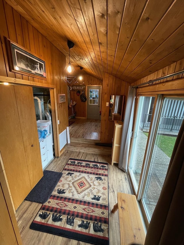 hall featuring lofted ceiling, light wood-type flooring, wood ceiling, and wooden walls