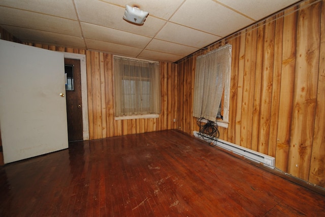 spare room with wood walls, hardwood / wood-style flooring, a baseboard heating unit, and a drop ceiling