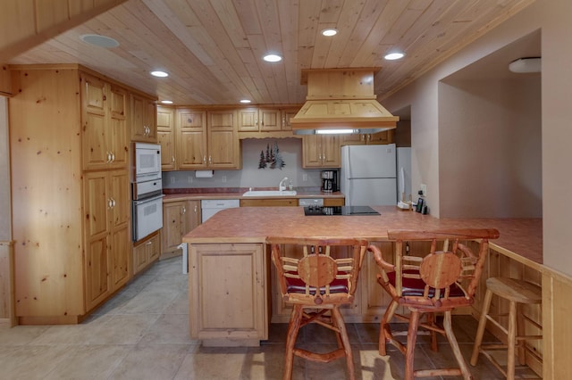 kitchen with custom exhaust hood, sink, white appliances, a kitchen breakfast bar, and light brown cabinets