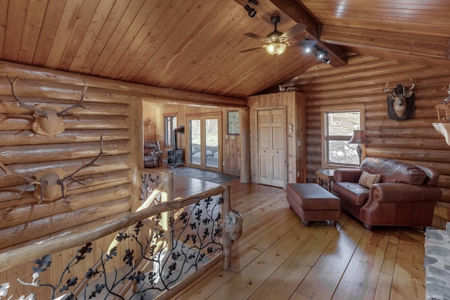 living room with ceiling fan, lofted ceiling with beams, rustic walls, and light hardwood / wood-style floors