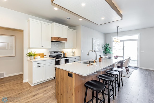 kitchen with sink, stainless steel electric stove, white cabinets, and a center island with sink