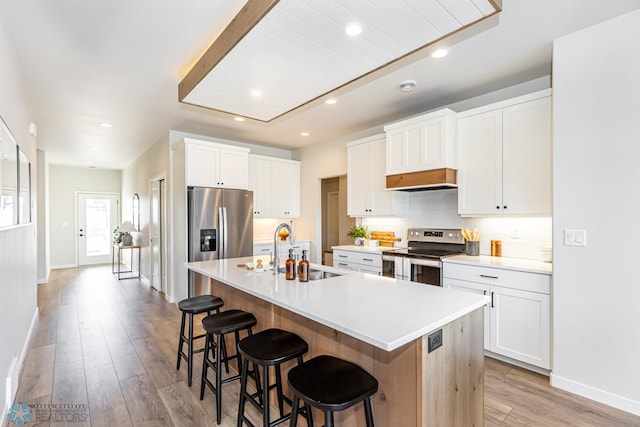 kitchen featuring a breakfast bar, white cabinetry, stainless steel appliances, light hardwood / wood-style floors, and an island with sink