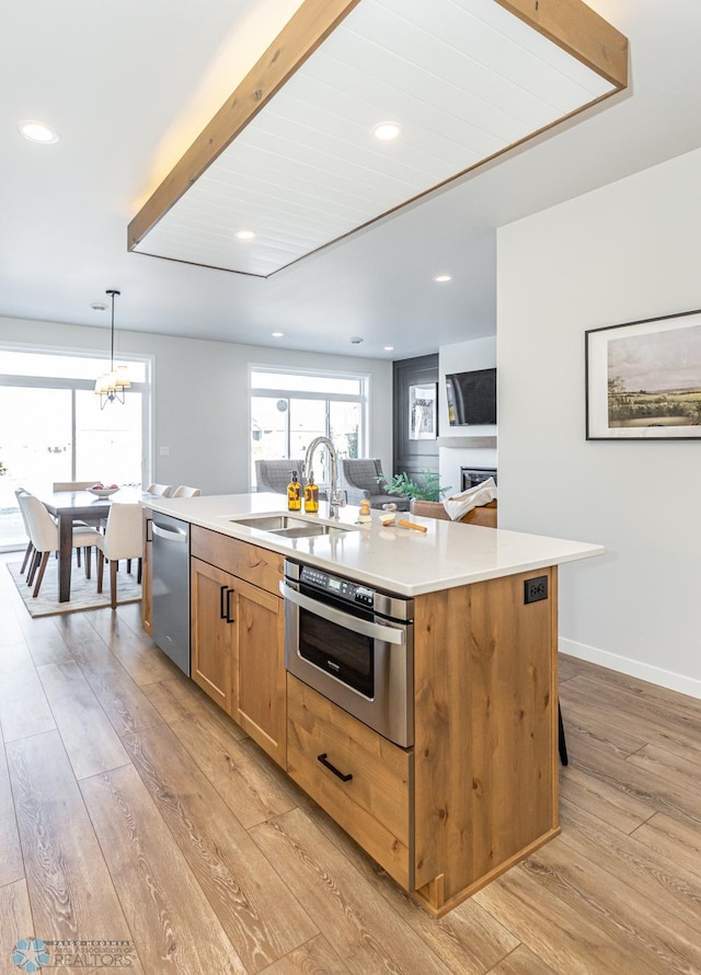 kitchen with pendant lighting, sink, a kitchen island with sink, light hardwood / wood-style floors, and oven