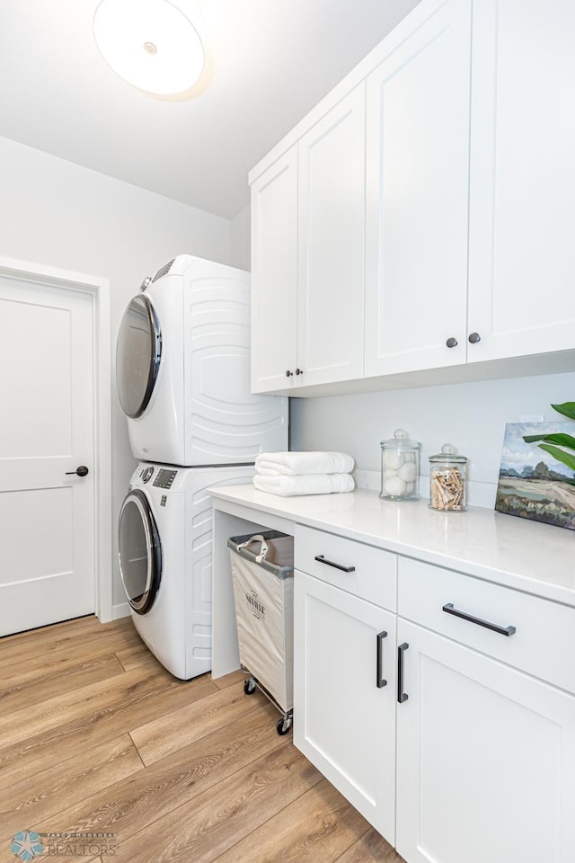 washroom featuring cabinets, stacked washing maching and dryer, and light hardwood / wood-style floors