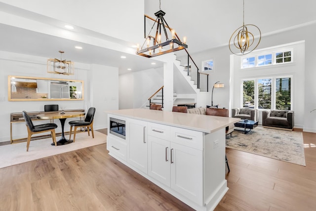 kitchen with light hardwood / wood-style flooring, white cabinetry, pendant lighting, stainless steel microwave, and a center island