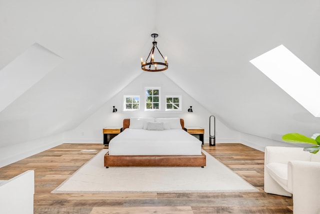 bedroom with lofted ceiling with skylight, a notable chandelier, and hardwood / wood-style flooring