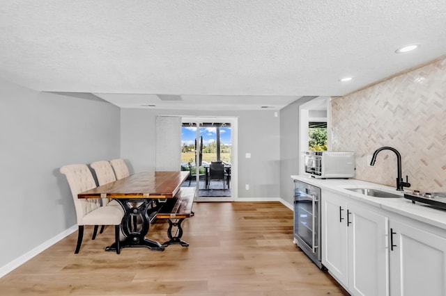 kitchen with sink, white cabinets, beverage cooler, and light wood-type flooring