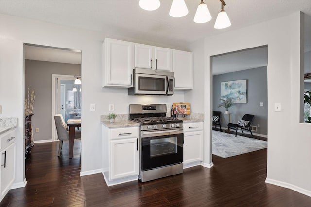 kitchen featuring pendant lighting, dark wood-type flooring, white cabinets, appliances with stainless steel finishes, and light stone counters