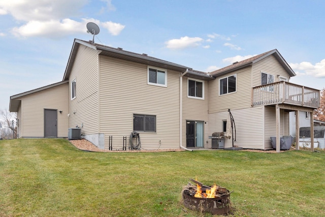 rear view of property featuring a wooden deck, an outdoor fire pit, cooling unit, and a lawn