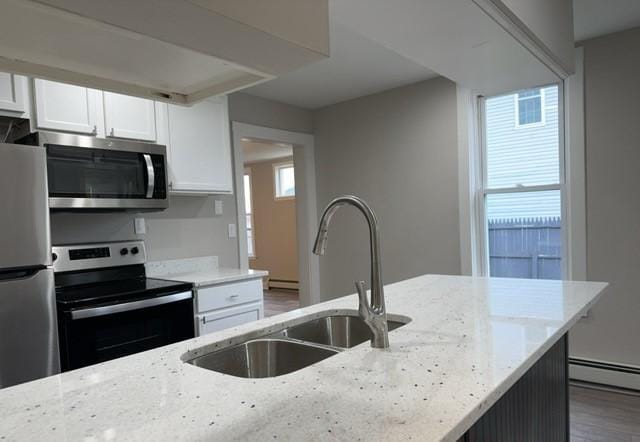 kitchen with light stone countertops, appliances with stainless steel finishes, a healthy amount of sunlight, and hardwood / wood-style floors