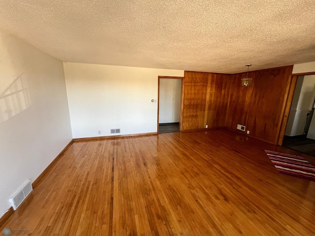 spare room with wooden walls, a textured ceiling, and hardwood / wood-style flooring