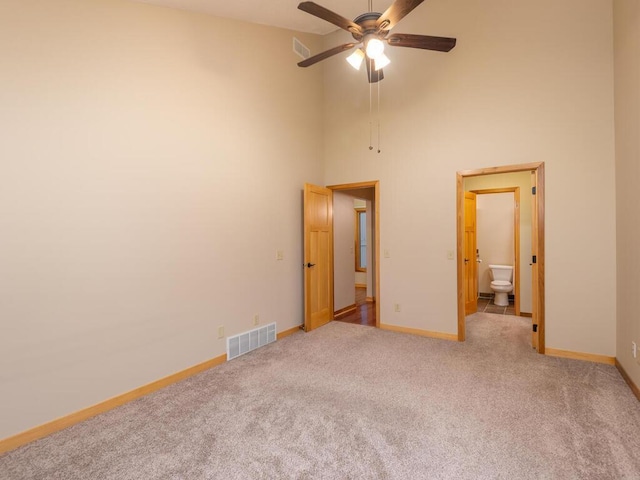 unfurnished bedroom featuring ceiling fan, light colored carpet, a towering ceiling, and ensuite bath