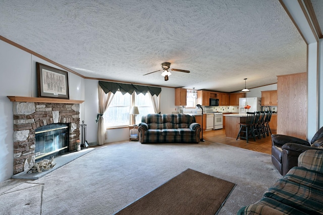 living room with light wood-type flooring, a textured ceiling, ceiling fan, crown molding, and a stone fireplace