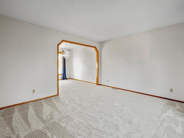 spare room featuring carpet, a notable chandelier, and a textured ceiling