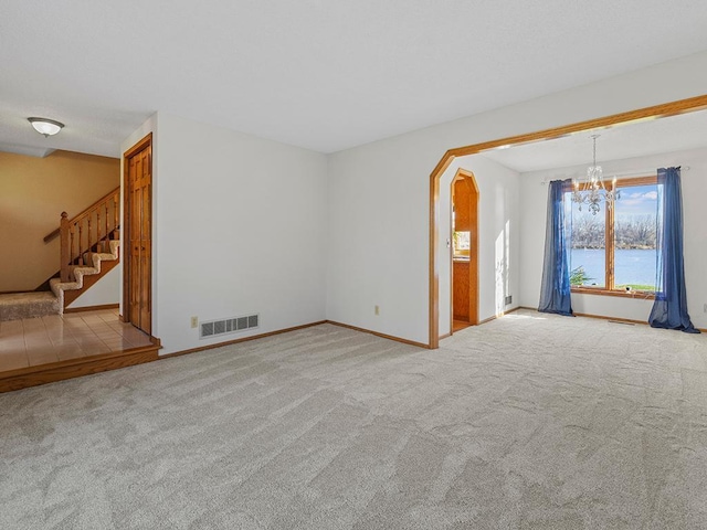 unfurnished living room featuring light colored carpet, an inviting chandelier, and a water view