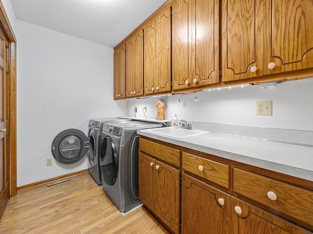 washroom featuring cabinets, sink, washer and dryer, light wood-type flooring, and a textured ceiling