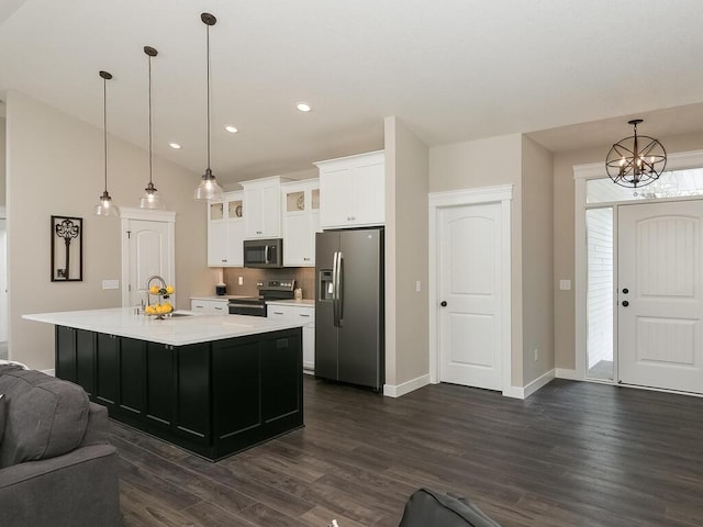 kitchen with appliances with stainless steel finishes, dark hardwood / wood-style flooring, decorative light fixtures, white cabinets, and an island with sink