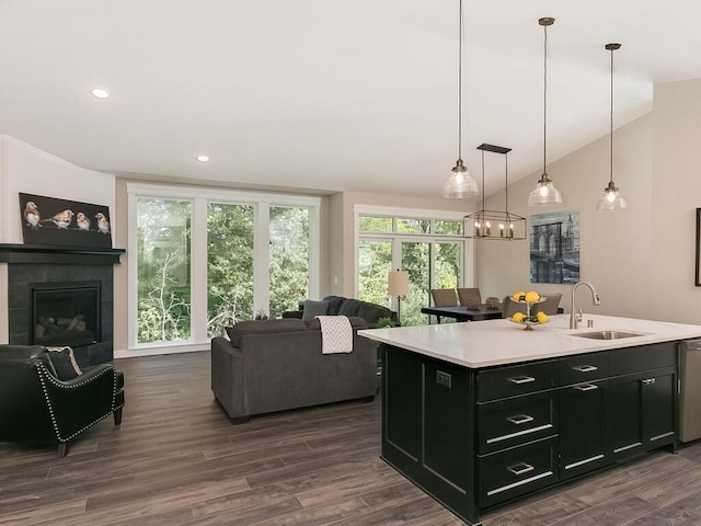 kitchen featuring sink, hanging light fixtures, an island with sink, vaulted ceiling, and a tiled fireplace