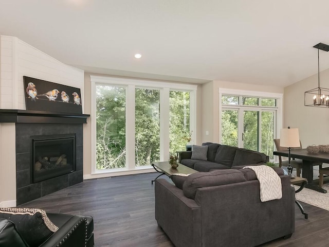 living room with a chandelier, lofted ceiling, dark wood-type flooring, and a tiled fireplace