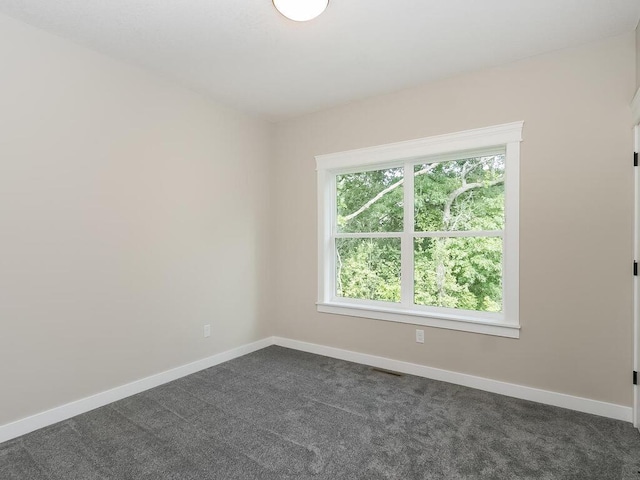 unfurnished room with a wealth of natural light and dark colored carpet