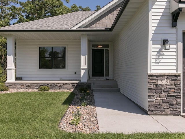 view of exterior entry featuring a lawn and a porch